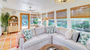 A spacious living room with a sectional sofa, a ceiling fan, and large windows with bamboo blinds. - Half-mi to Private Beach: Floridana Beach Getaway (Melbourne Beach)