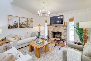 A living room with a fireplace, white sofas, a coffee table, and artwork on the wall.