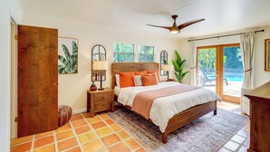 A bedroom with a wooden bed, a nightstand, a mirror, and a view of a pool through a glass door. - Half-mi to Private Beach: Floridana Beach Getaway (Melbourne Beach)