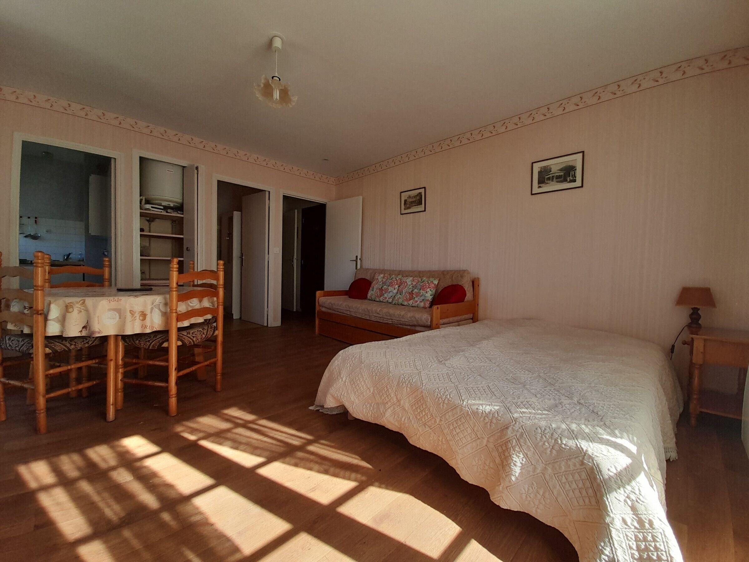 A bedroom with a bed, a wooden chair, a table, and a sofa. There are doors leading to other rooms.