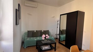 A bedroom with a bed, a small table with a vase, a mirror, and a wardrobe.