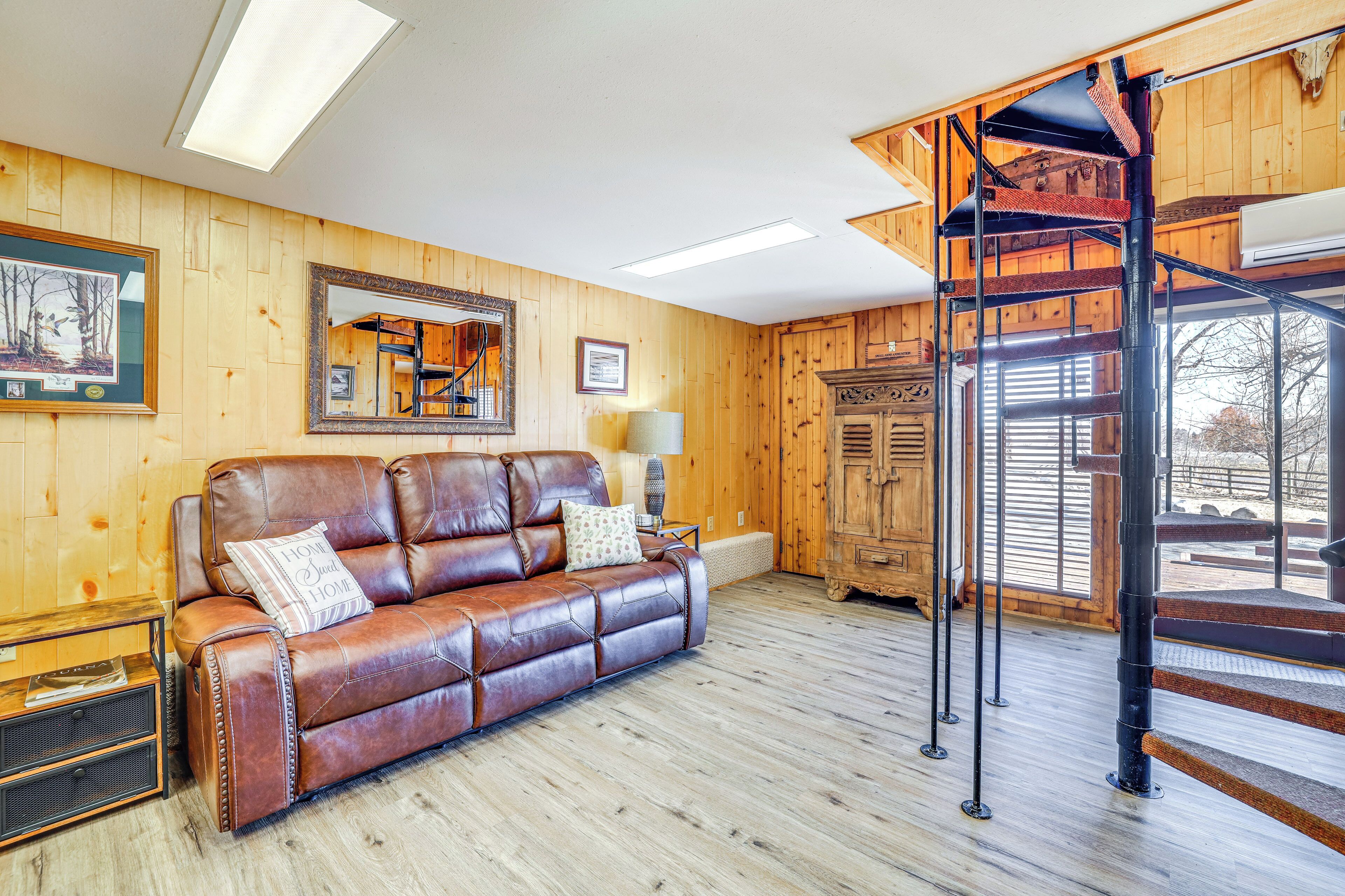 A wooden-paneled room with a leather sofa, a mirror, a staircase, and a wooden cabinet.