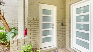 A building exterior with a white door and windows, brick walls, and some greenery. - Pasture & Pond Views: Lovely Lutz Apartment (Lutz)