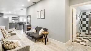 A modern living room with a grey sofa, a small round table, and a kitchen in the background. - Pasture & Pond Views: Lovely Lutz Apartment (Lutz)