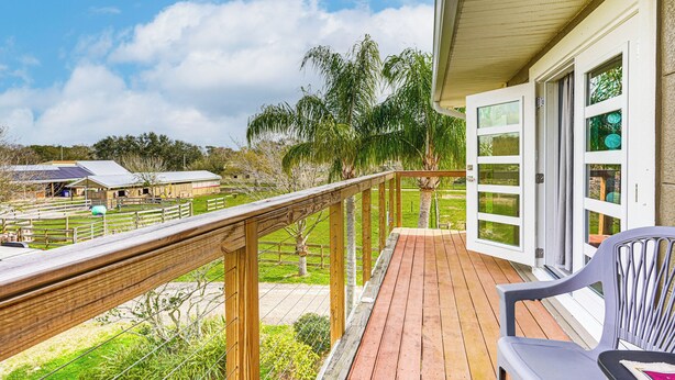 A wooden deck with a railing, a chair, and a view of a farm and trees. - Pasture & Pond Views: Lovely Lutz Apartment (Lutz)