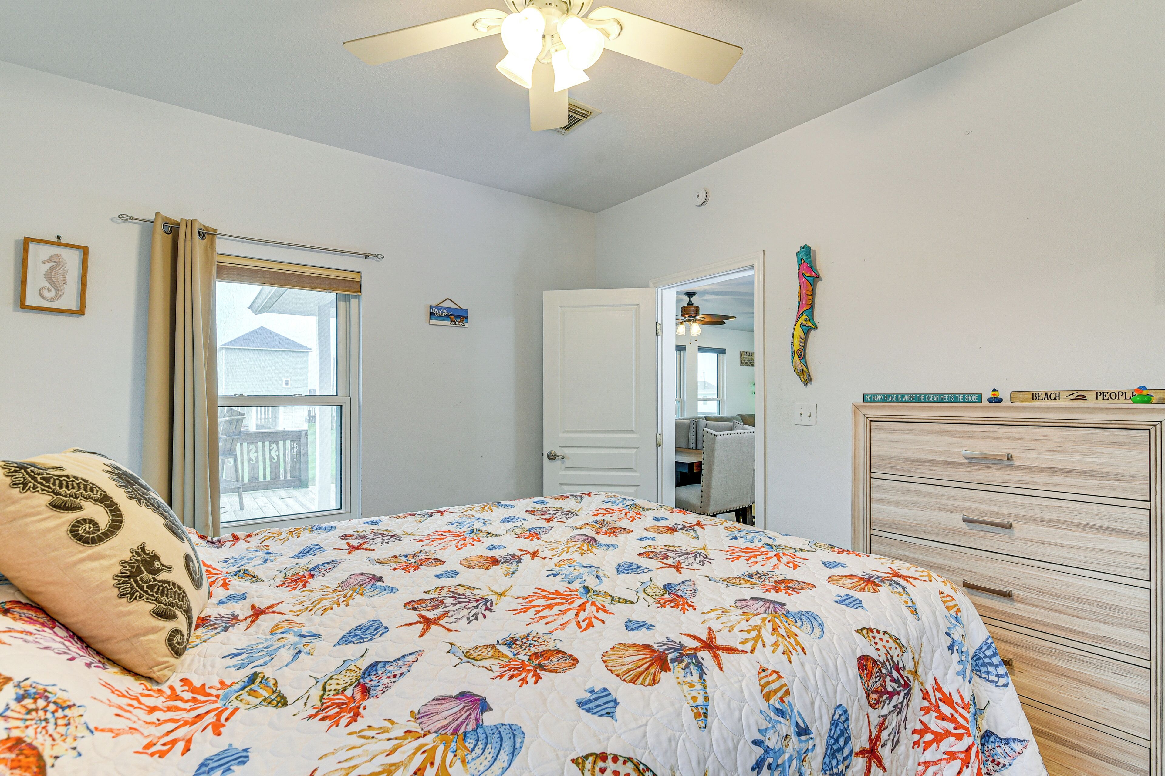 A bedroom with a bed, a ceiling fan, a window with curtains, a door, and a dresser.