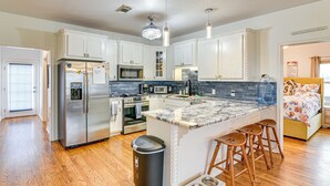 A modern kitchen with white cabinets, stainless steel appliances, a marble countertop, and a built-in island with stools. - Near Surfside Jetty County Park: Home w/ Deck! (Freeport)