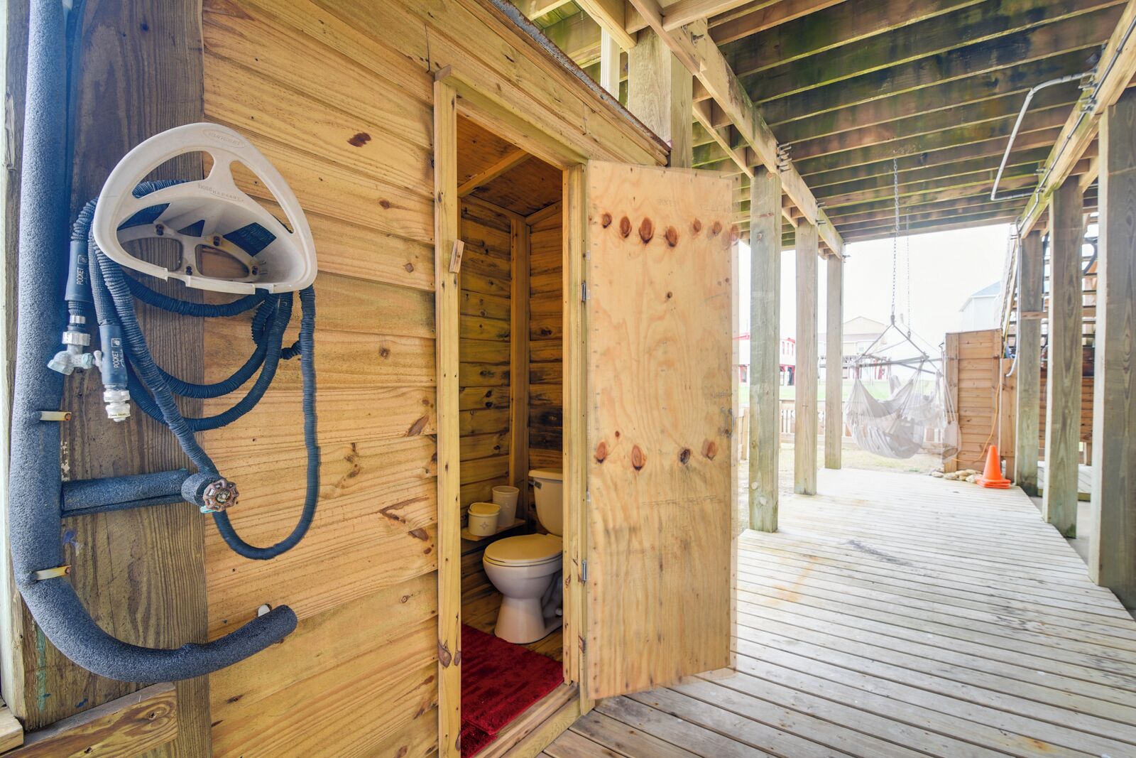 Uma cabana de madeira com um banheiro pequeno, incluindo vaso sanitário e área de chuveiro com mangueiras.