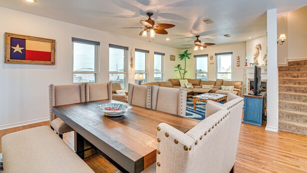 A spacious living room with a large wooden dining table, beige upholstered chairs, and a ceiling fan. - Near Surfside Jetty County Park: Home w/ Deck! (Freeport)