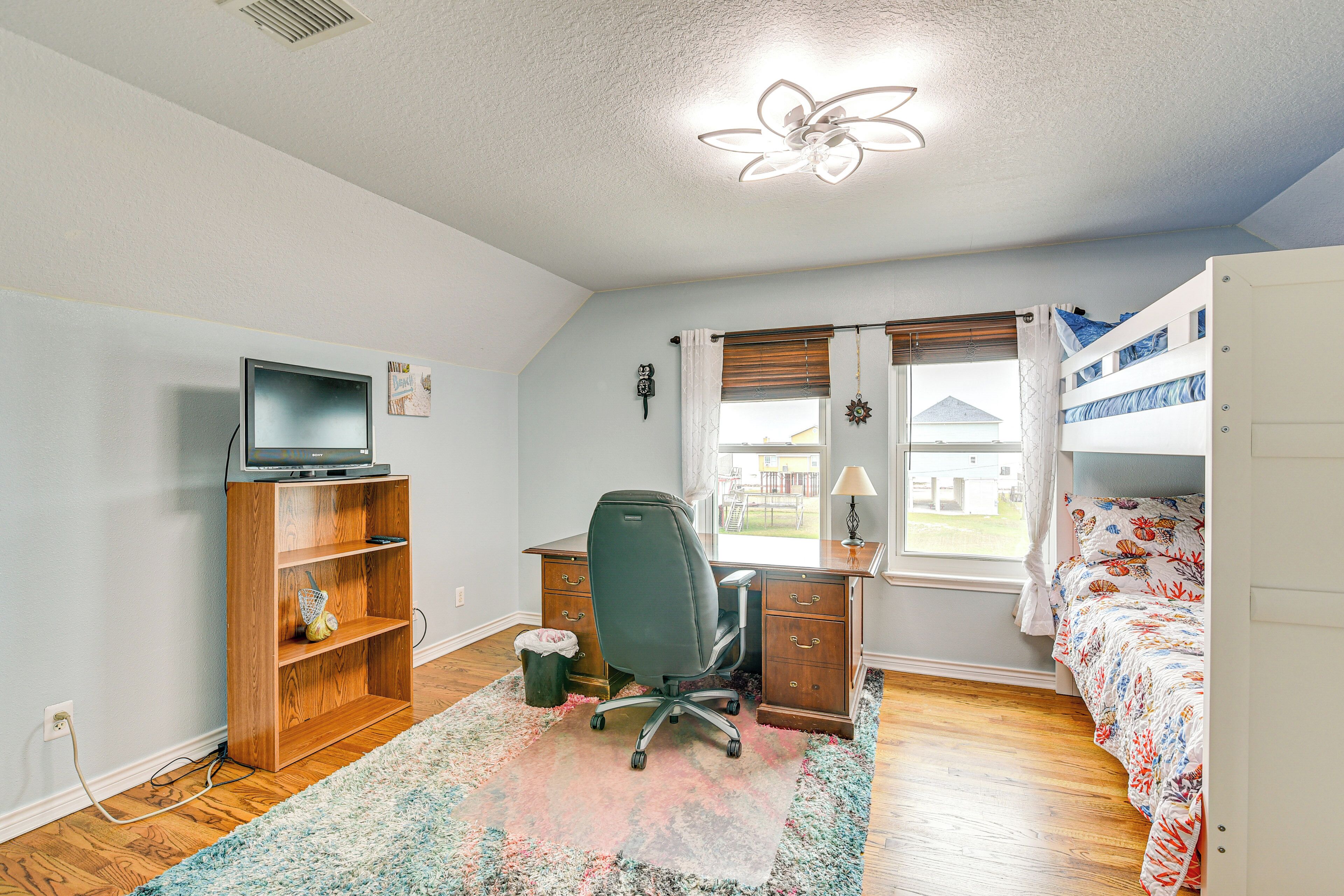 A bedroom with a desk, chair, bunk bed, and a window with blinds.