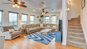 A spacious living room with a large sectional sofa, a coffee table, and a ceiling fan. There is a staircase leading to another level. - Near Surfside Jetty County Park: Home w/ Deck! (Freeport)