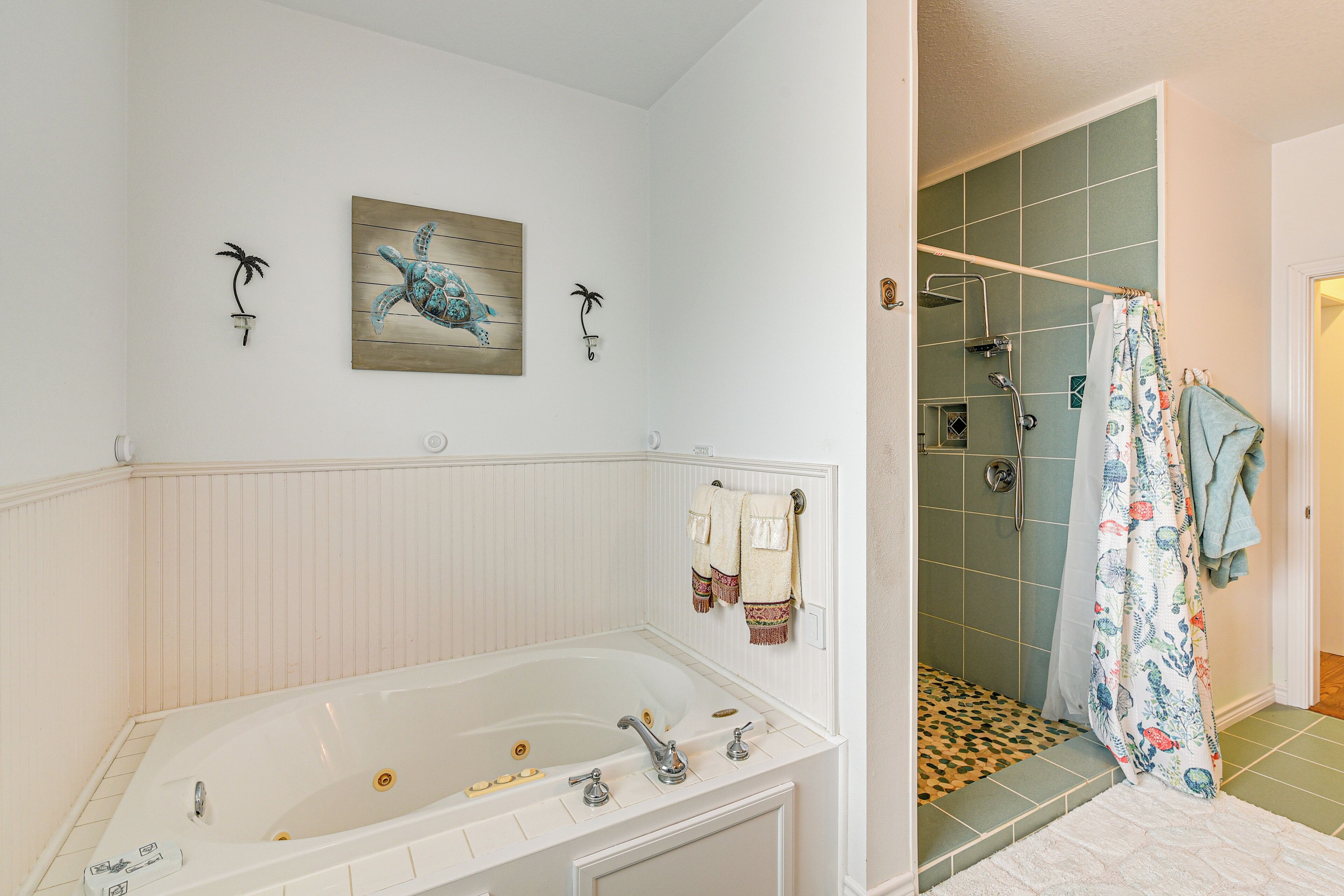A bathroom with a large bathtub, a shower with a patterned curtain, and wall-mounted towels.