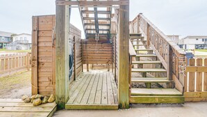 A wooden staircase leading to a covered area with a metal railing. - Near Surfside Jetty County Park: Home w/ Deck! (Freeport)