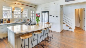 A modern kitchen with a large island, bar stools, and a view of the outside through large windows.