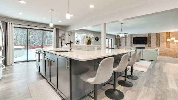 A modern kitchen with a large island, bar stools, and a dining area with a light-colored table and chairs. - 3 Mi to Dtwn Alpena: Family Home w/ Yard! (Alpena)