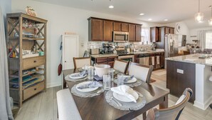 A modern kitchen with wooden cabinets, stainless steel appliances, and a dining area set for six with a large island. - 1 Mi to Colonial Beach Boardwalk: Home w/ Fire Pit (Colonial Beach)