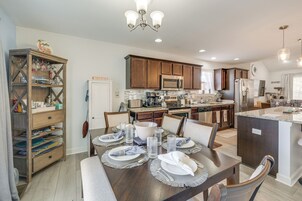 Cozinha moderna com armários de madeira, eletrodomésticos de aço inoxidável e uma sala de jantar para seis pessoas, com uma bancada grande.