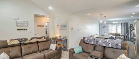 A spacious living room with two brown leather sofas, a ceiling fan, and a dining area with a table and chairs.