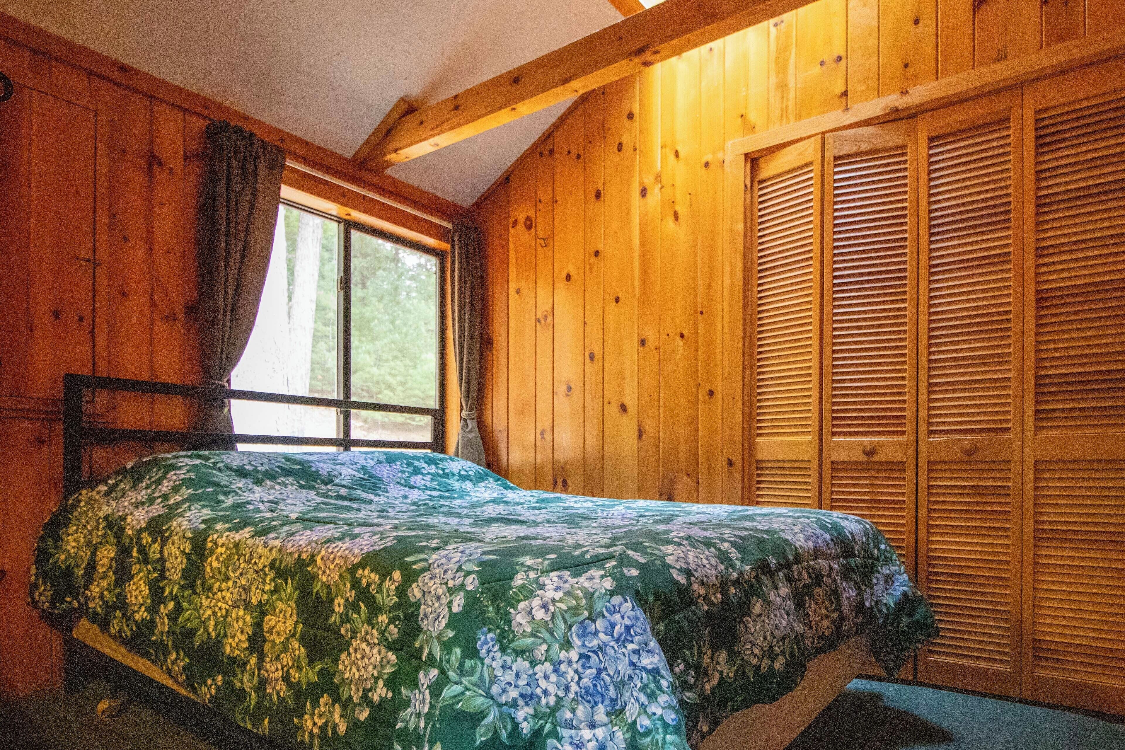 A wooden cabin bedroom with a bed, a window, and a wooden closet.