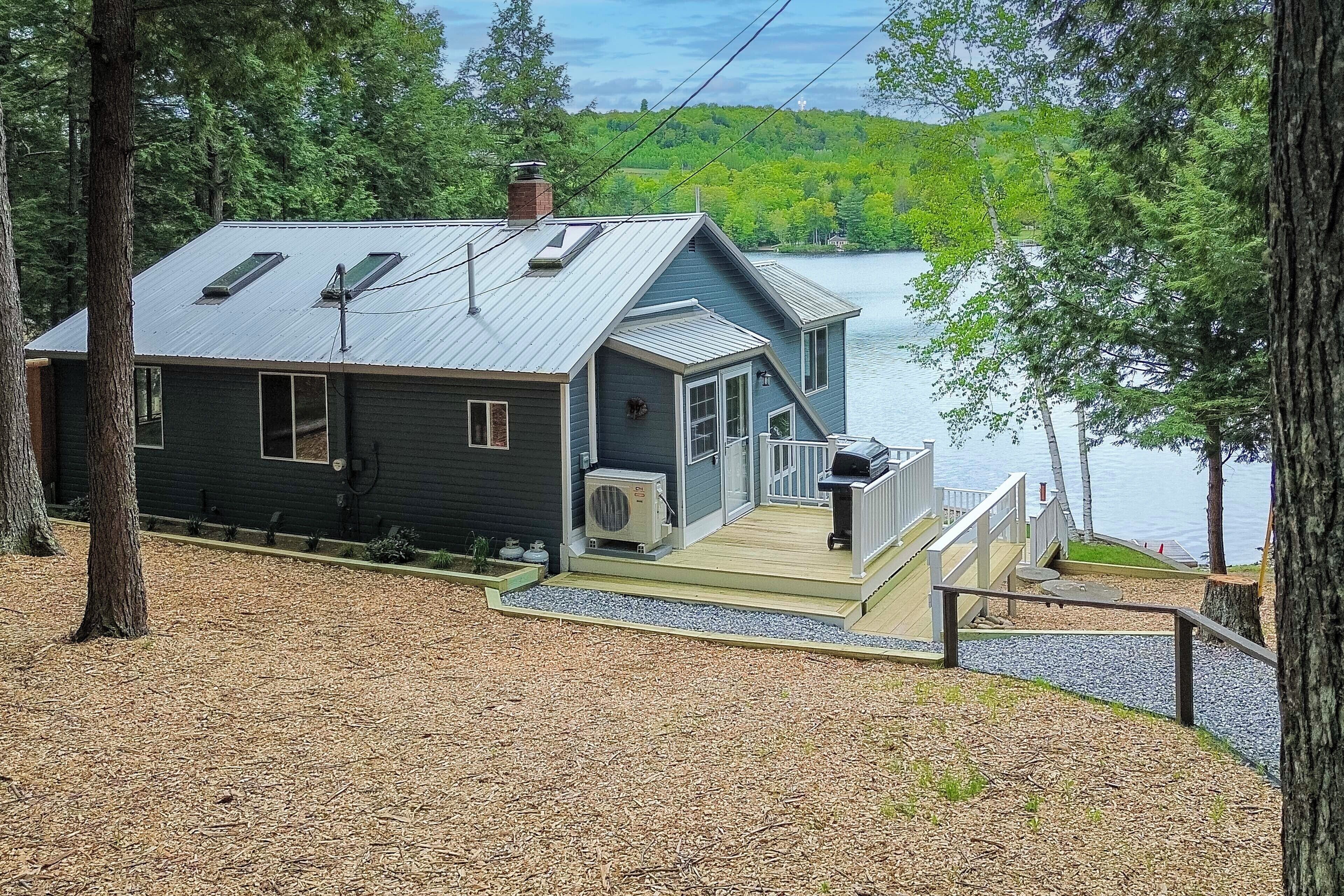 A cabin with a deck, a chimney, and a view of a lake.
