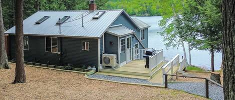 A cabin with a deck, a chimney, and a view of a lake.