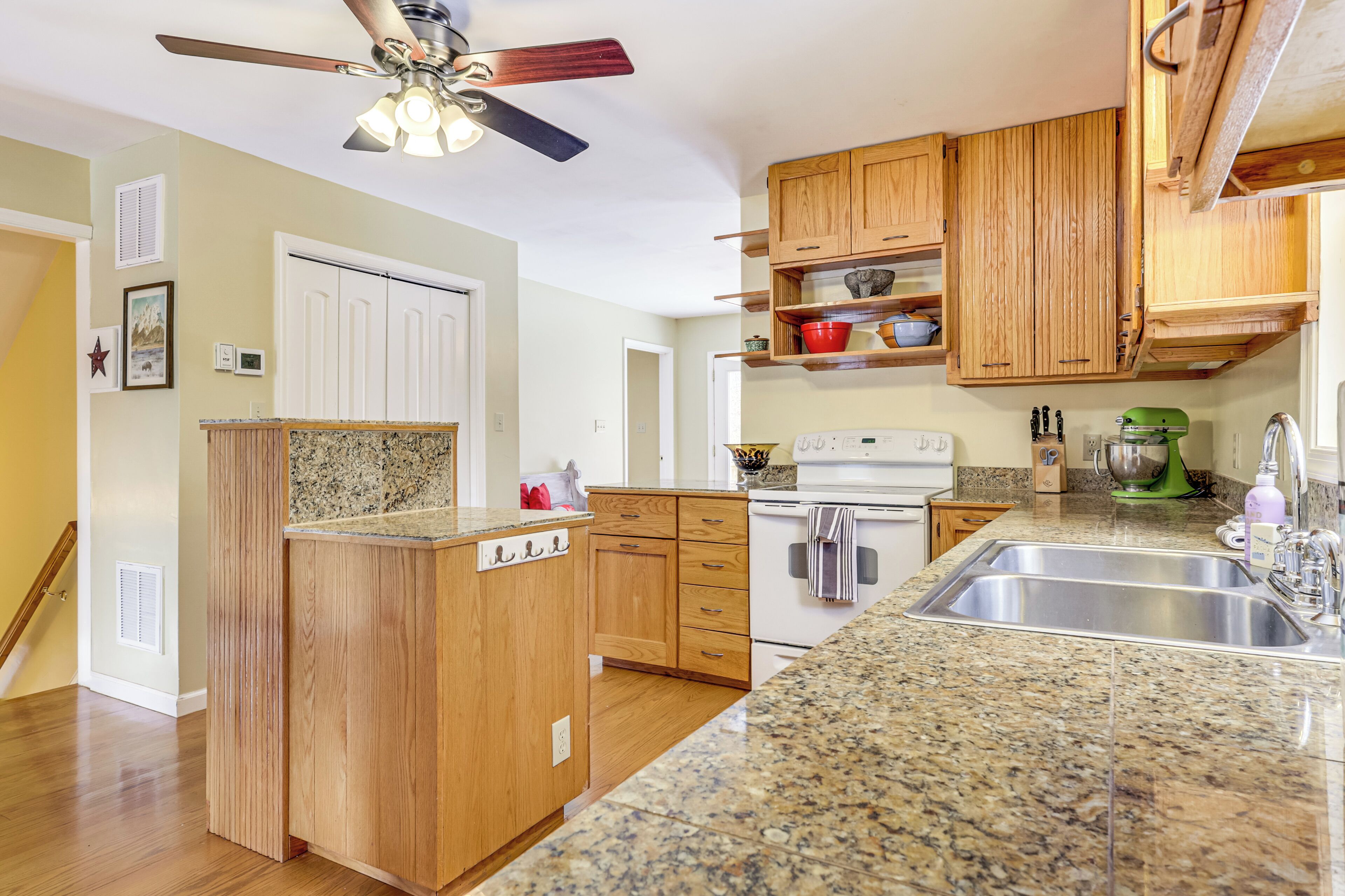 A kitchen with wooden cabinets, granite countertops, a built-in oven, and a ceiling fan.