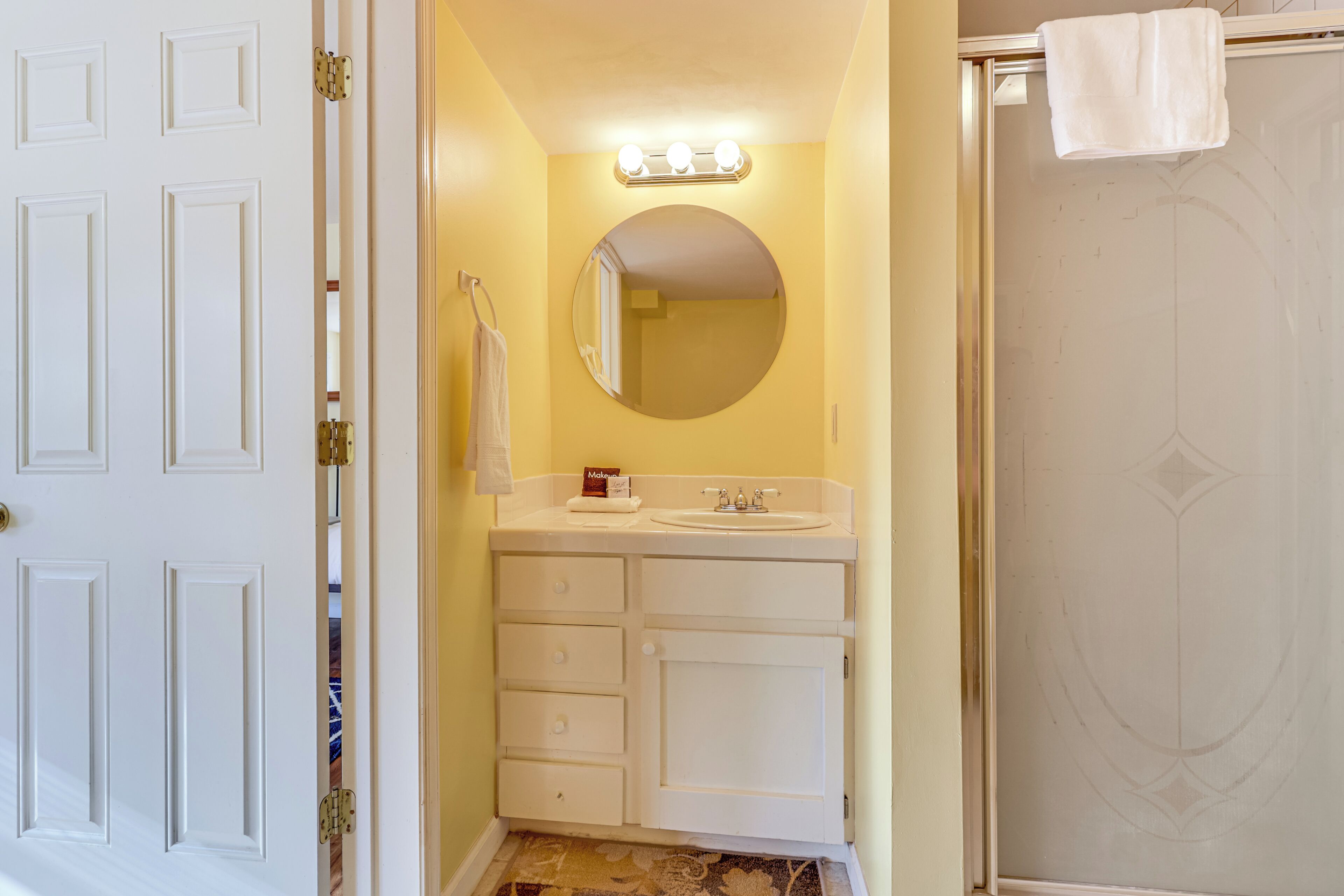 Ein Badezimmer mit weißem Waschtisch, einem runden Spiegel und einer Dusche mit Glastür.