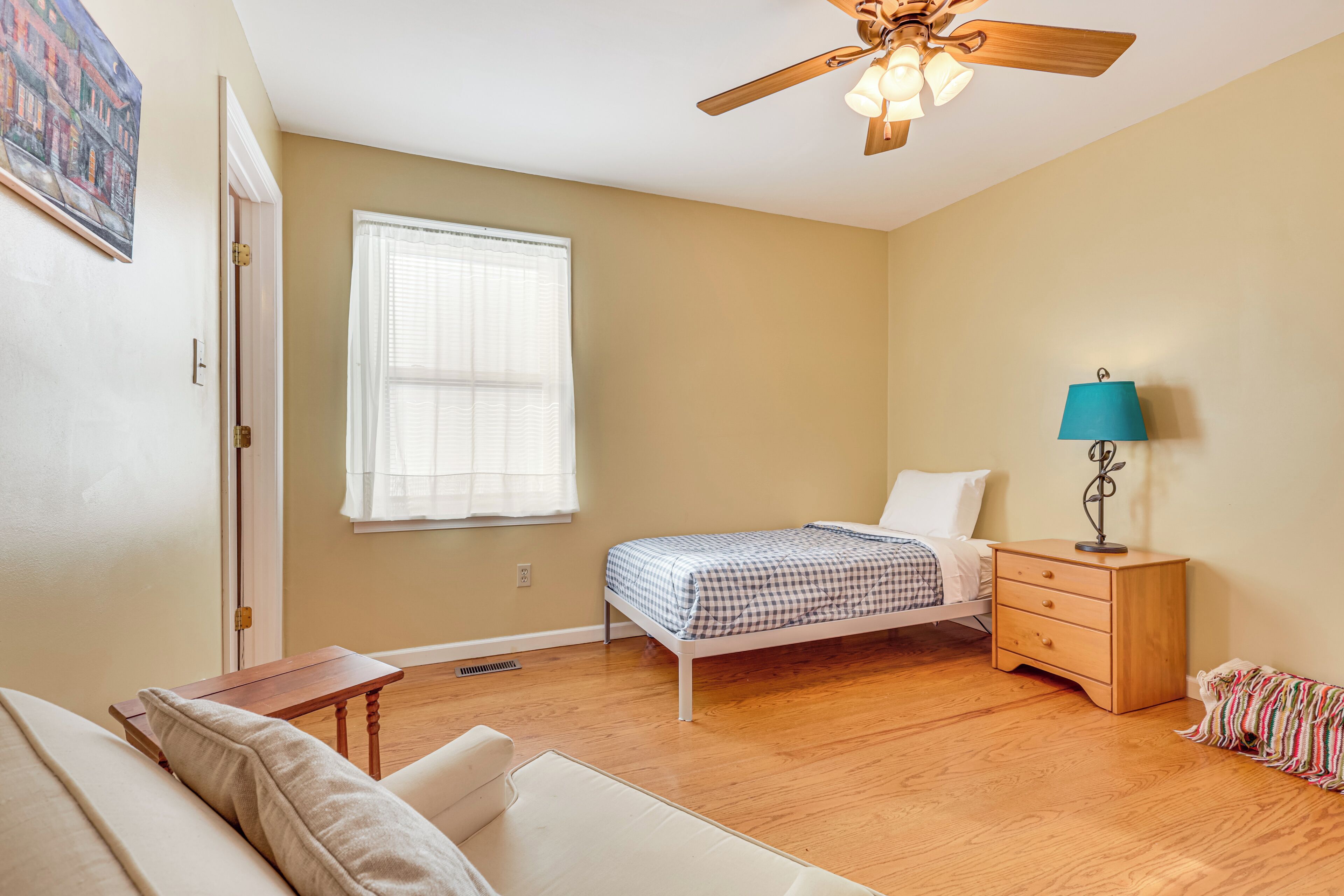 A bedroom with a bed, a nightstand, a lamp, a ceiling fan, and a window.