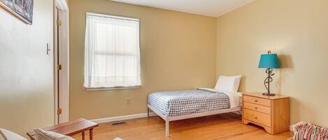 A bedroom with a bed, a nightstand, a lamp, a ceiling fan, and a window.