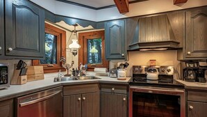 A kitchen with dark wooden cabinets, stainless steel appliances, and a red-tiled backsplash. - Ramona Point on 4th Lake (Old Forge)