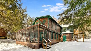 A cabin with a glass enclosure, wooden deck, and a green door. - Ramona Point on 4th Lake (Old Forge)