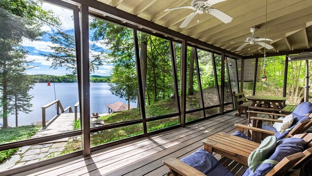 A covered deck with wooden furniture and a view of a lake. - Ramona Point on 4th Lake (Old Forge)