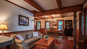 A cozy living room with a wooden ceiling, a sofa, a coffee table, and a dining area with a table and chairs. - Ramona Point on 4th Lake (Old Forge)