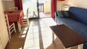 Un espacio habitable compacto con comedor, sofá, televisor y balcón.