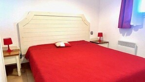 Un dormitorio con una cama grande, paredes blancas y una ventana con cortinas moradas.