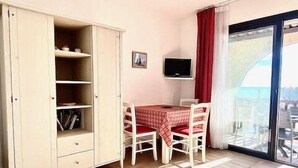 Una habitación pequeña y bien iluminada con una mesa de comedor, sillas, un armario, un televisor y un amplio ventanal con vistas.