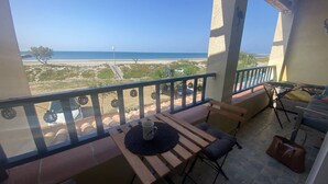 Ein Balkon mit Blick auf den Strand, ein Tisch mit Unterlage und Tasse sowie ein Stuhl.