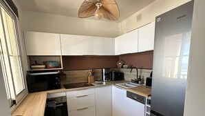 Eine moderne Küche mit weißen Schränken, einem Edelstahlkühlschrank, einer Mikrowelle und einem Essbereich mit einem Stuhl.