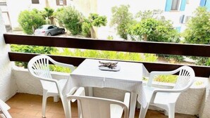 Eine kleine Terrasse im Freien mit einem Tisch und vier weißen Plastikstühlen, umgeben von einem Hollerdgeschoss.