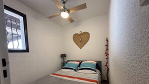 Ein Schlafzimmer mit Bett, Deckenventilator, Wanddekoration in Herzform und einem Fenster mit Gitter.