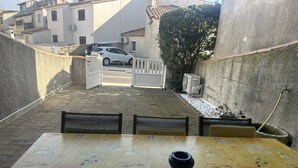 Un pati exterior amb una taula i cadires, una porta i un cotxe al fons.