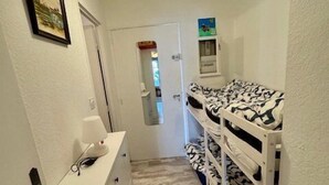 A narrow hallway with bunk beds on the right, a desk with a lamp on the left, and a door at the end. - Studio-type apartment with terrace and parking space (SAINTES MARIES DE LA MER)