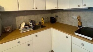 A kitchen with white cabinets, a wooden countertop, and a black electric kettle. - Studio-type apartment with terrace and parking space (SAINTES MARIES DE LA MER)