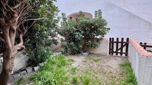 A courtyard with a white building, a tree, and a small bush. - Studio-type apartment with terrace and parking space (SAINTES MARIES DE LA MER)