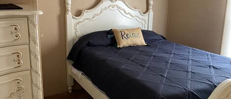Une chambre à coucher avec un lit à baldaquin blanc, une couette bleu foncé et un coussin orné du mot «
Relax
».