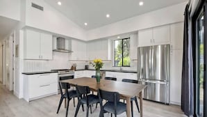 A modern kitchen with white cabinetry, a central island with seating, and stainless steel appliances. - Private Cardiff Beach House (Encinitas)