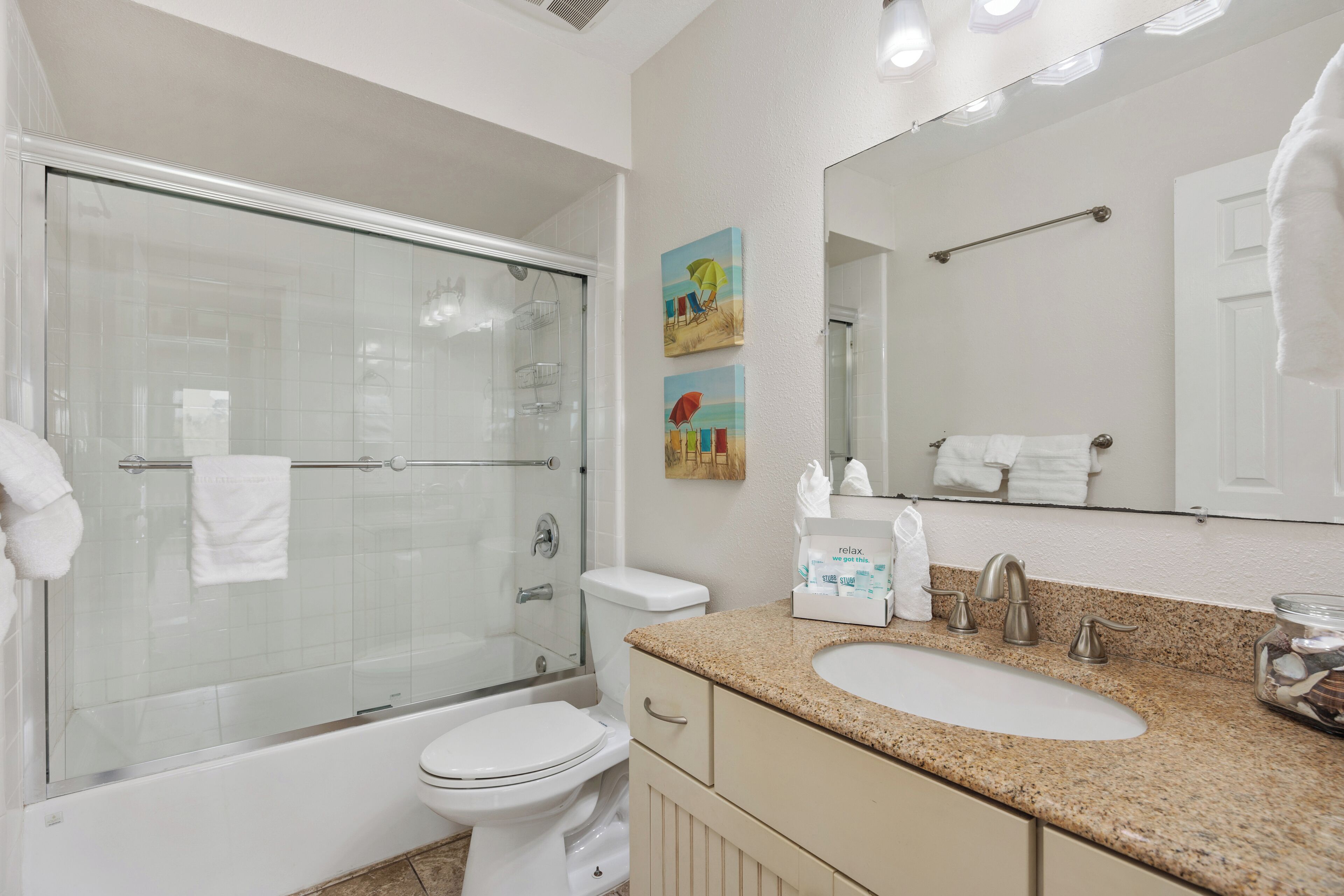 A bathroom with a glass-enclosed shower, a toilet, a sink with a granite countertop, and a mirror.