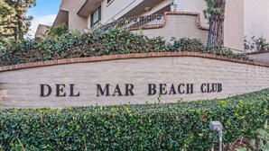 Fasaden på Del Mar Beach Club med en tydlig skylt, en mur av tegel och en välskött häck.