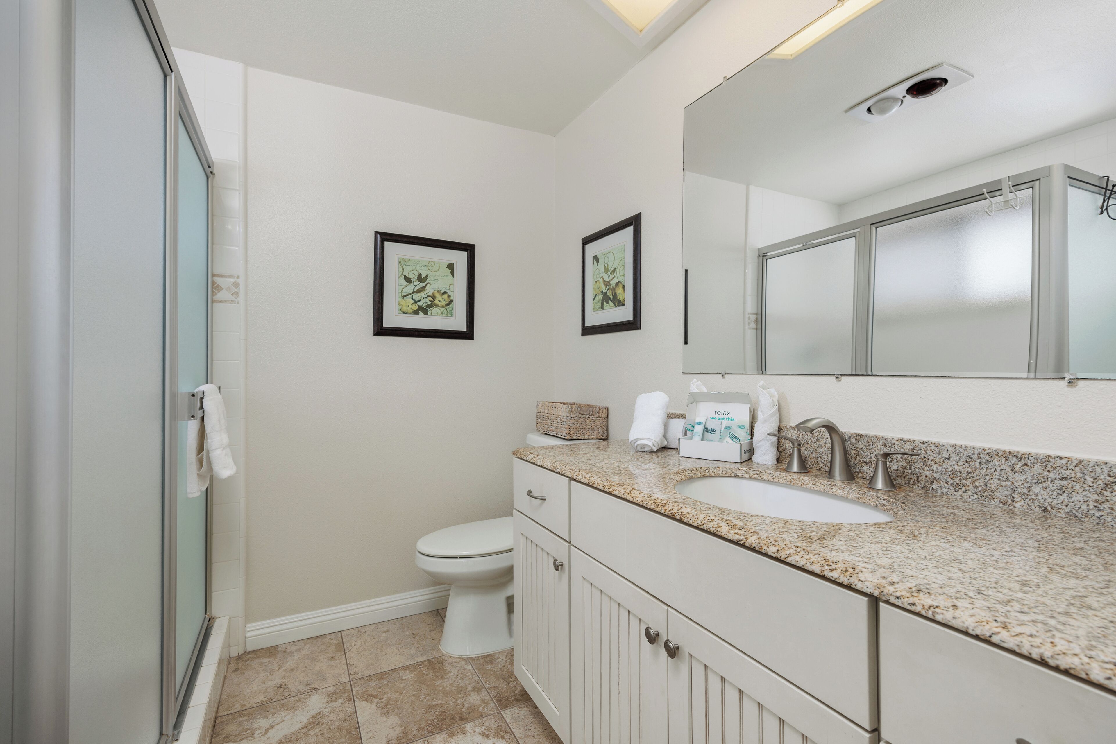 A bathroom with a shower, toilet, sink, and two framed pictures on the wall.