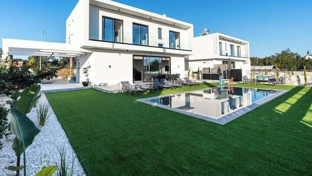 Een modern huis met twee verdiepingen, een zwembad, een overdekt terras en een keurig onderhouden gazon.